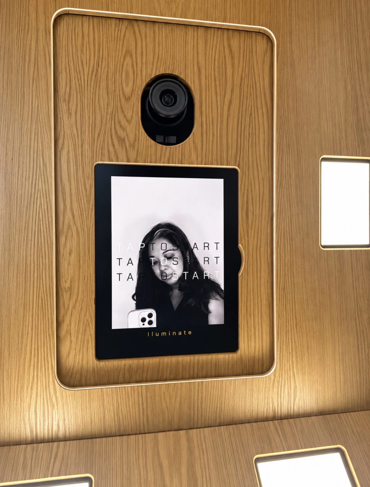 Wooden photo booth with a camera and portrait screen, retaining its original Illuminate markings