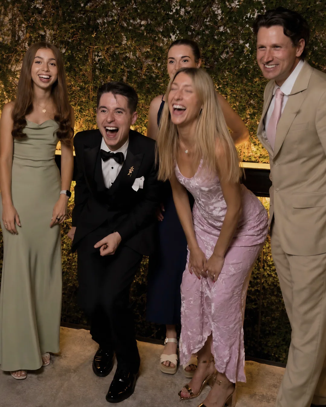 Wedding guests laugh together in front of the leafy backdrop
