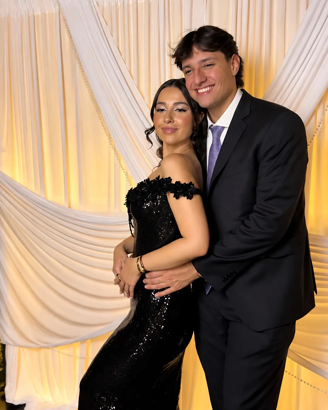 Two guests pose together against the softly lit draped backdrop