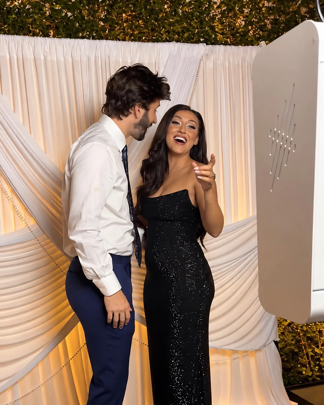Two guests laugh in front of the draped backdrop