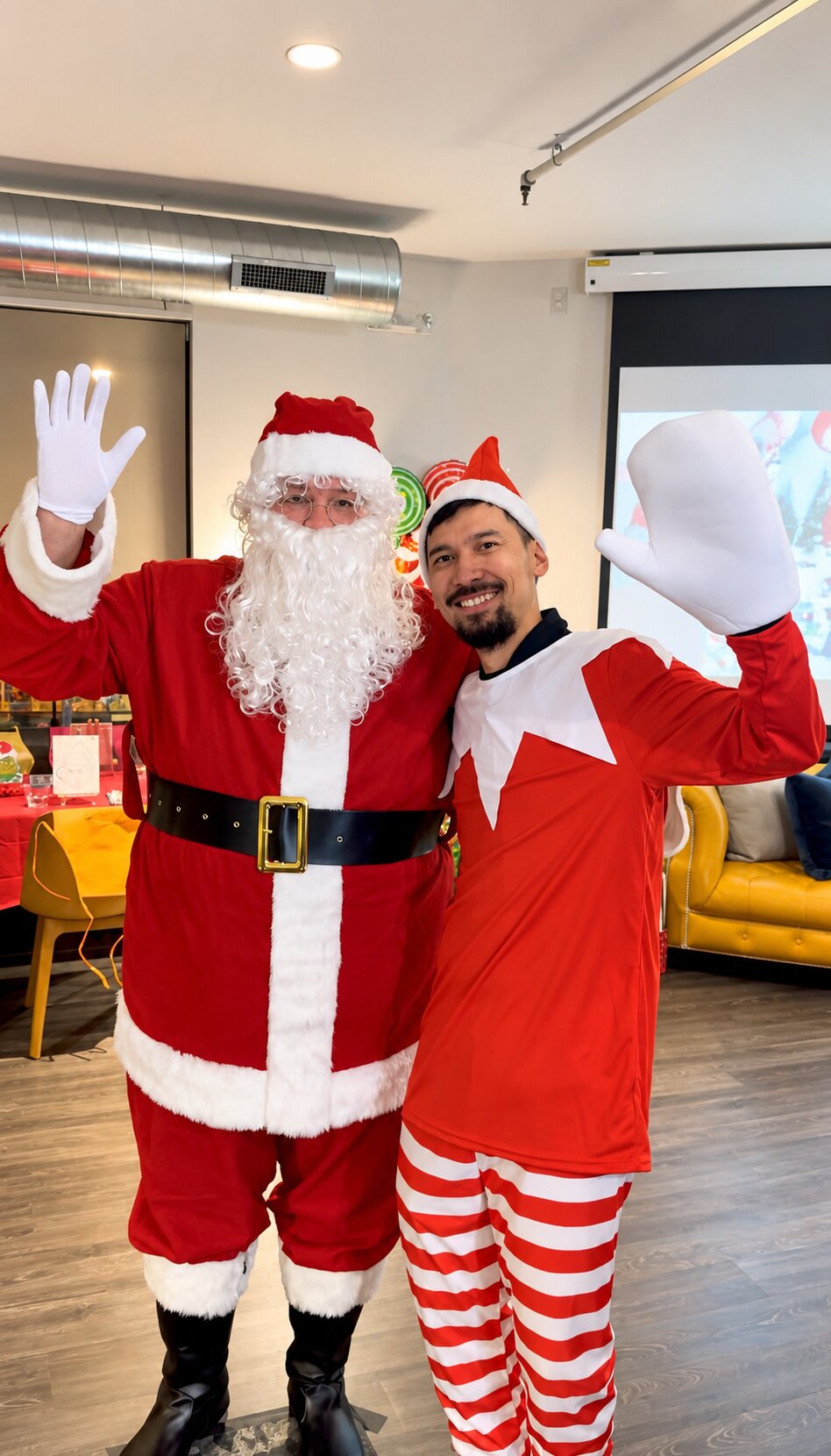 Santa and a guest in red holiday attire waving together