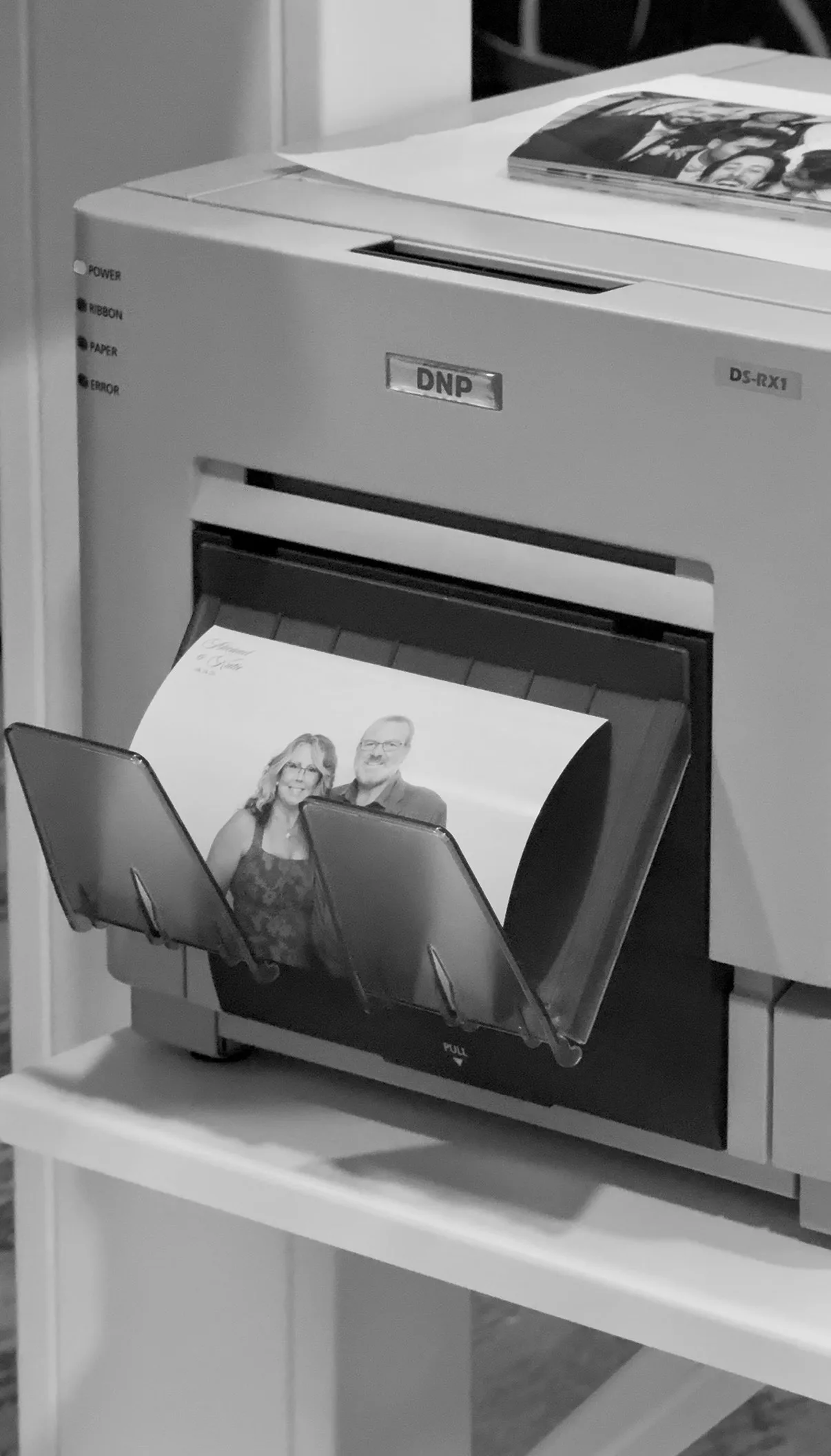 A photo of two guests emerges from the Glam Booth printer